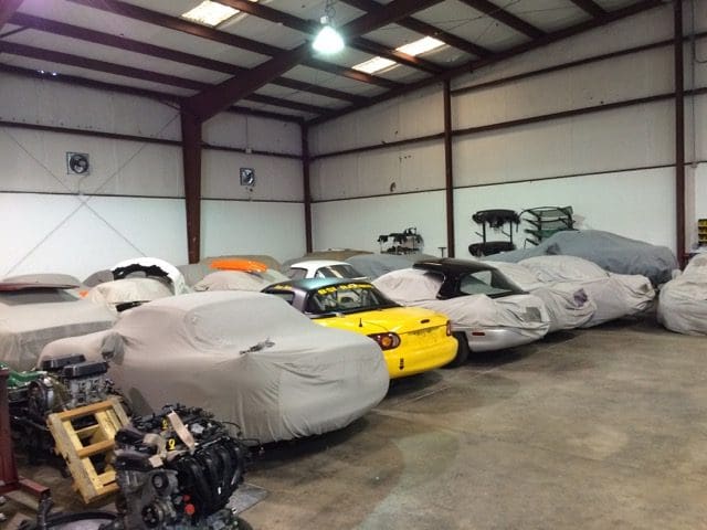 A warehouse with many cars covered in tarps.
