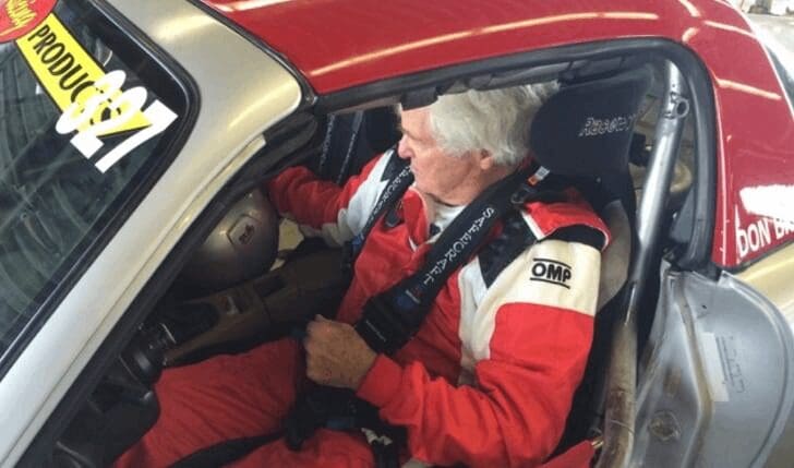 An older man sitting in the driver's seat of a race car captures the essence of fine art.