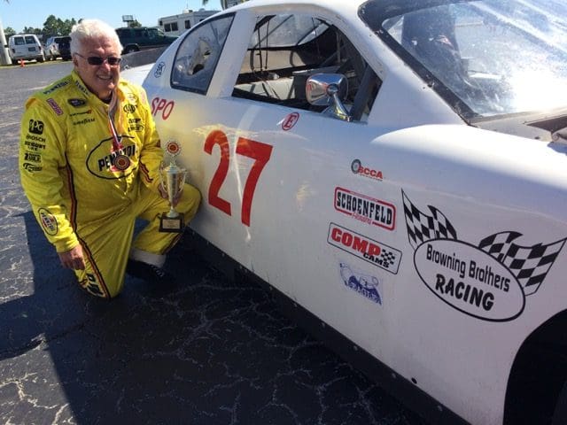 A man in yellow standing next to a white race car.