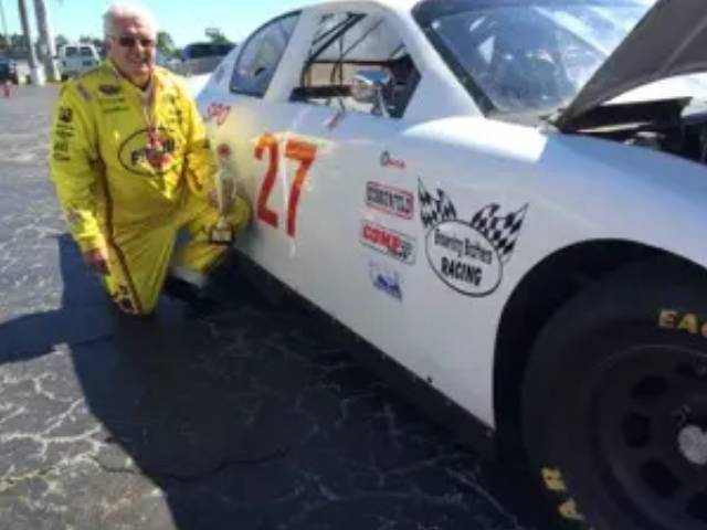 A man in yellow overalls next to a white race car.