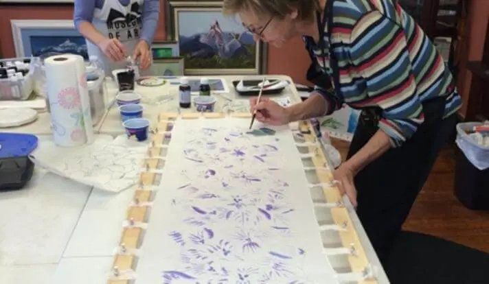 A woman painting flowers on paper with purple paint.