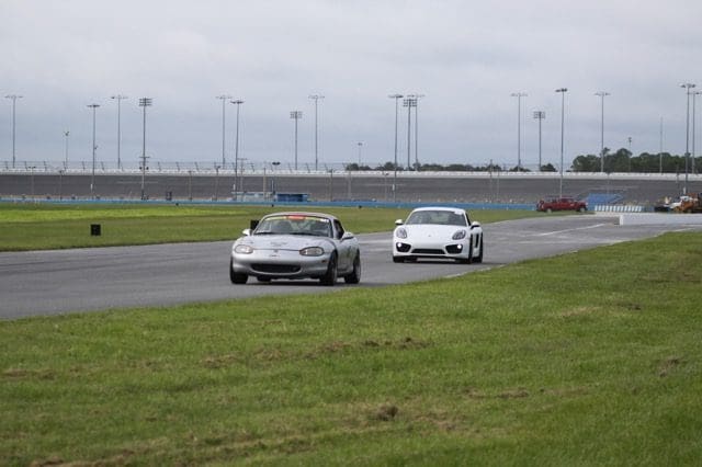 Two cars are driving on a track near some grass.