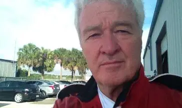 A man in red jacket standing next to trees.