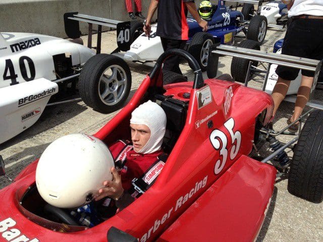 A man in a red race car sitting in the driver 's seat.
