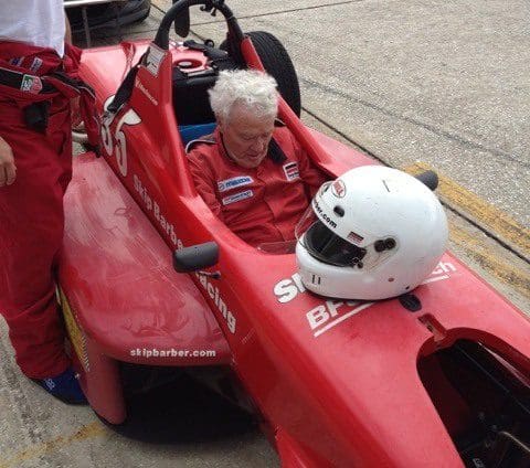 A man sitting in the back of an old red race car.