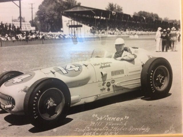 A man in an old race car driving on the track.