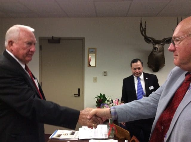 Two men shaking hands in a room with a wall mounted deer head.
