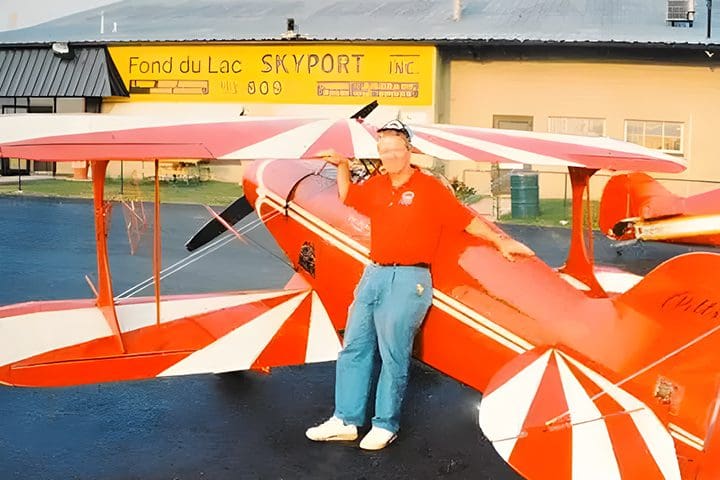 A man standing next to an airplane in front of the sign.