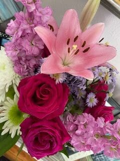 Capture the elegance of pink lilies paired with purple flowers in a vase.