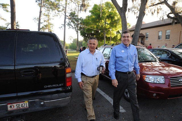 Two men walking in a parking lot next to some cars.