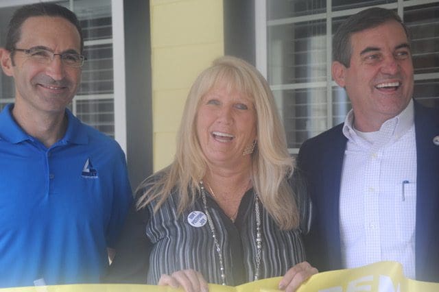 A woman standing next to two men holding a yellow ribbon.