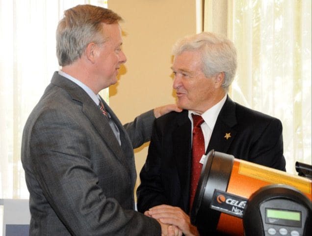 Two men shaking hands in front of a machine.