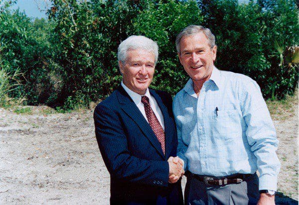 Two men shaking hands in front of trees.